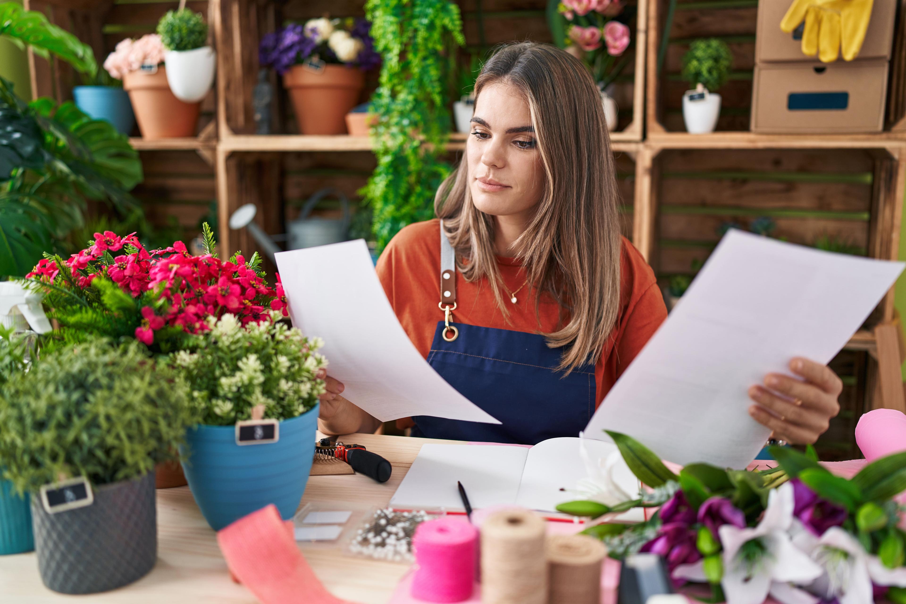 Photo d'une fleuriste lisant des documents sur une table de son atelier - Accompagnement entreprise en bretagne