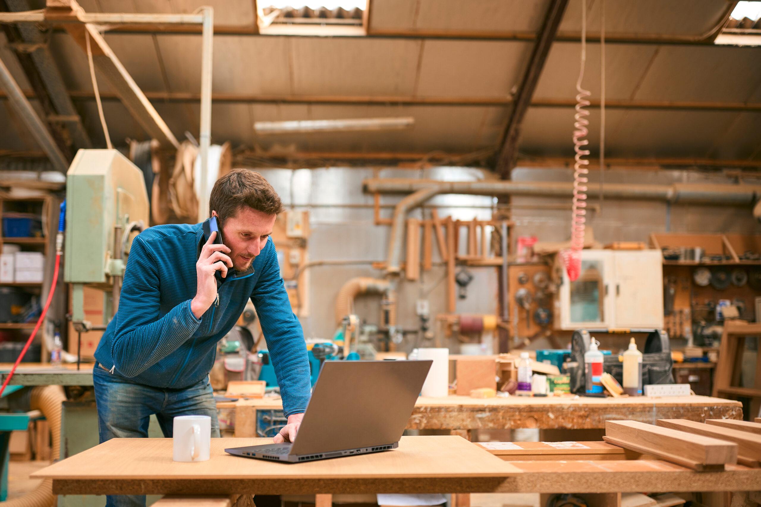Menuisier travaillant dans un atelier parlant au téléphone et utilisant un ordinateur portable - Financer son BFR